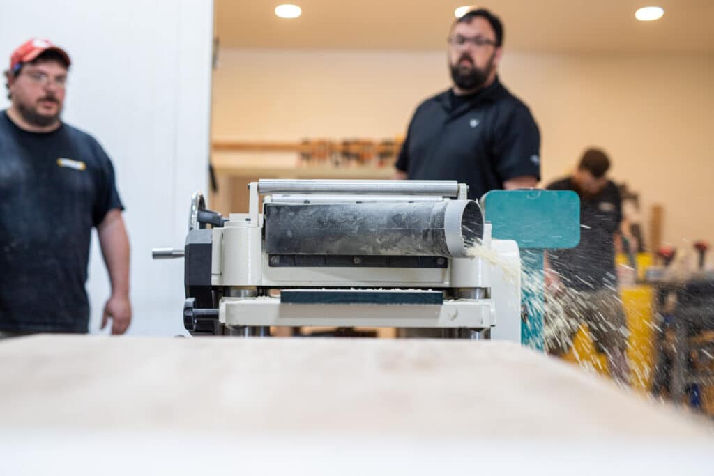 Adam Tressner, Owner & Founder of TressCo Construction, and TressCo team member using a planer on a piece of wood to be used in custom cabinetry.